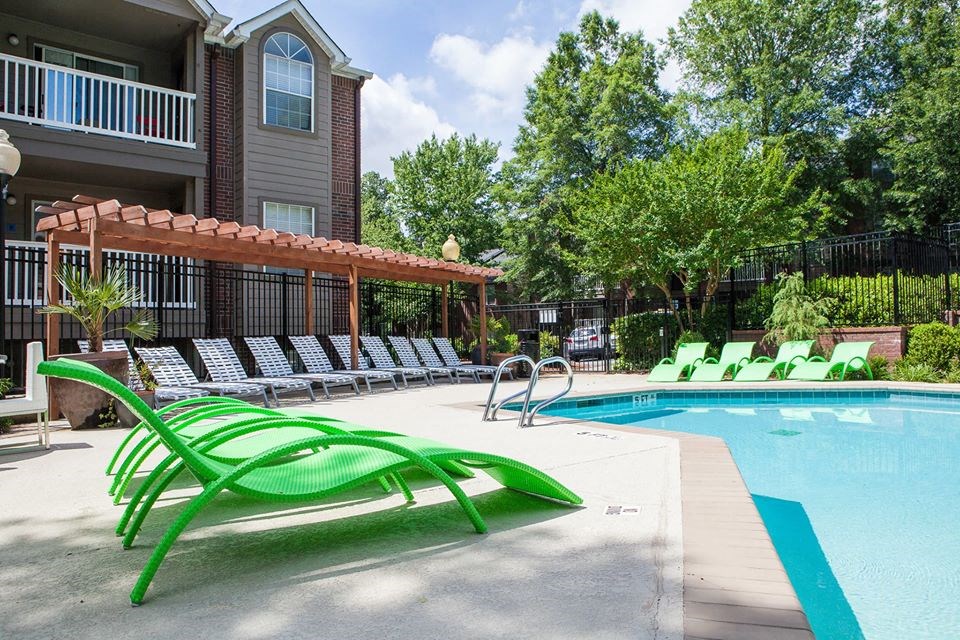 a swimming pool with green chairs next to a building