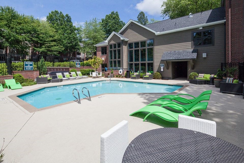 a swimming pool with green chairs in front of a house