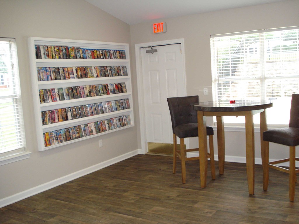 a dining room with a table and chairs and a bookshelf filled with movies