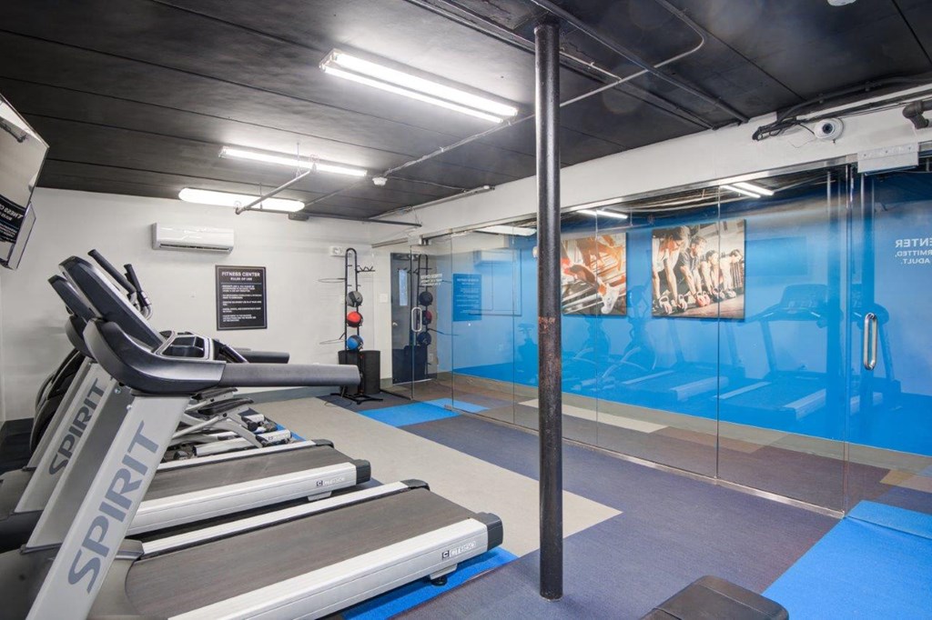 a gym with a treadmill and weights in a room with a glass door