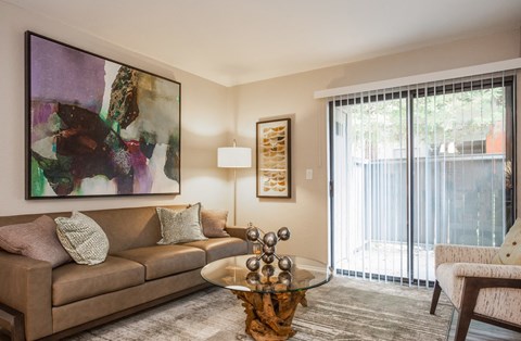 A living room with a brown couch, a glass coffee table, and a painting on the wall.
