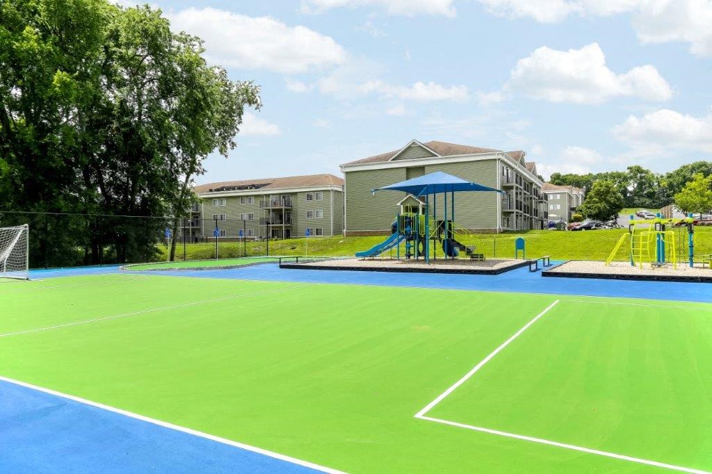 a tennis court with a playground and a swing set in front of a building