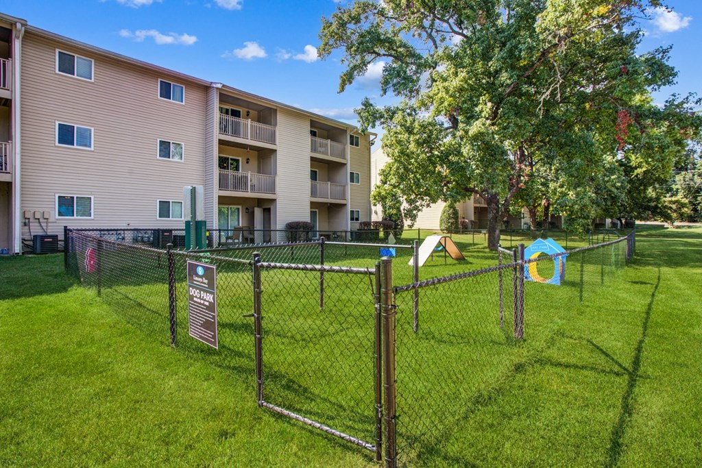 a fenced in dog park in front of an apartment building