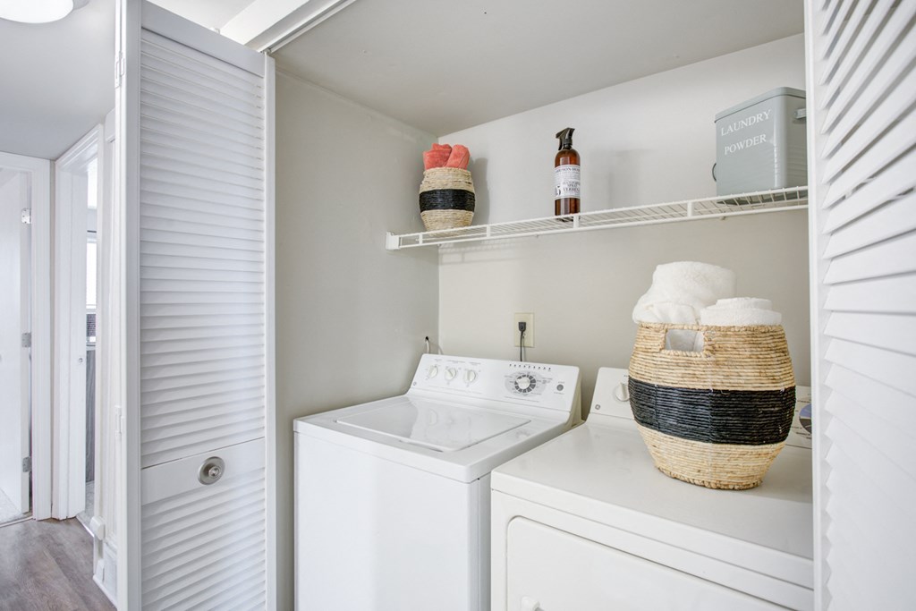 a white washer and dryer in a white laundry room with a shelf above
