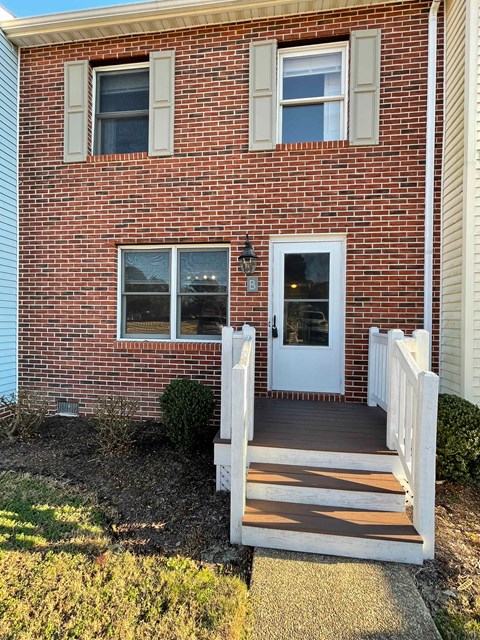A red brick house with a white door and steps leading to it.