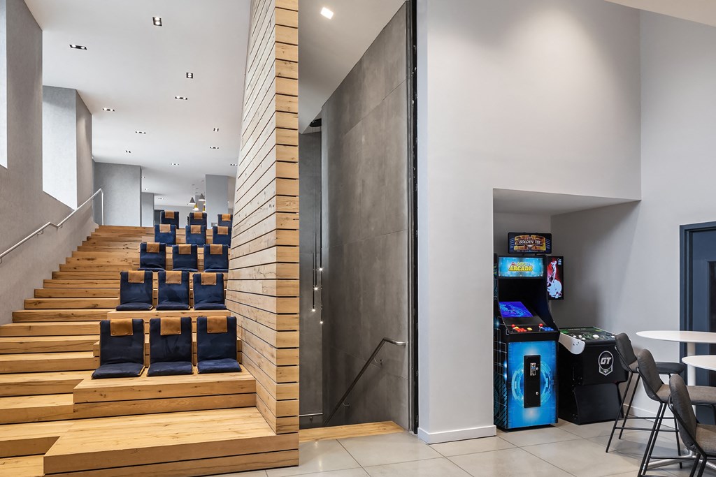 a lobby with stairs and chairs and a video game and a vending machine
