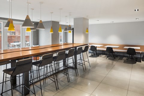 a communal area with tables and chairs and a bar with chairs