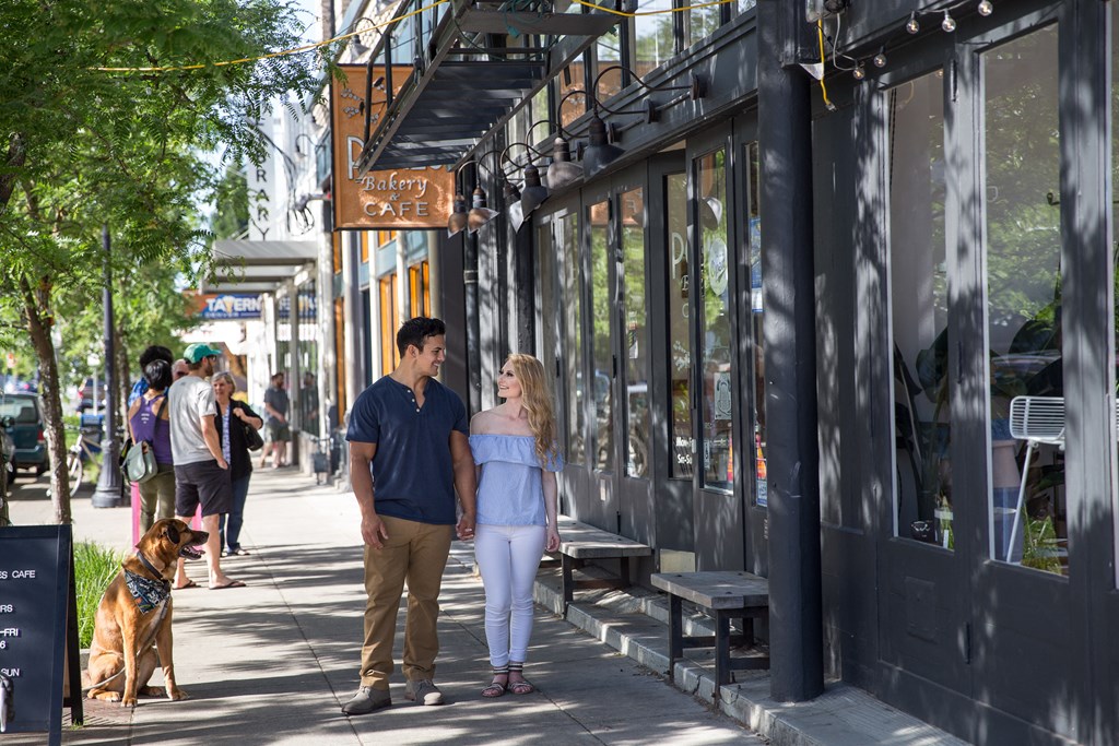 a man and woman walking down a sidewalk with a dog