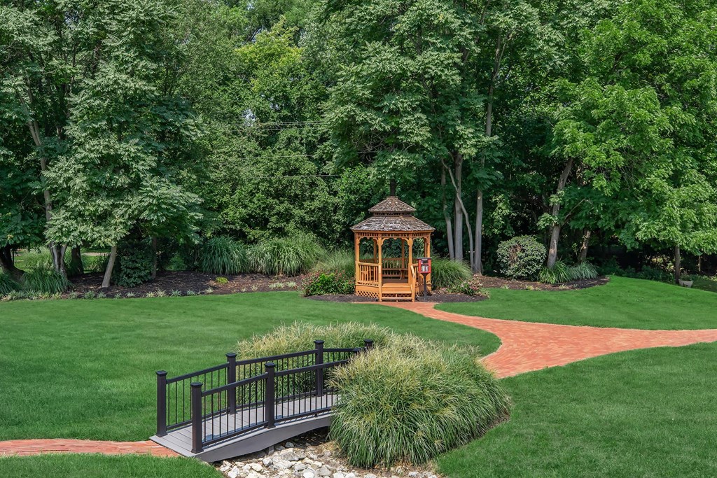 a gazebo in the middle of a yard with a bridge over a