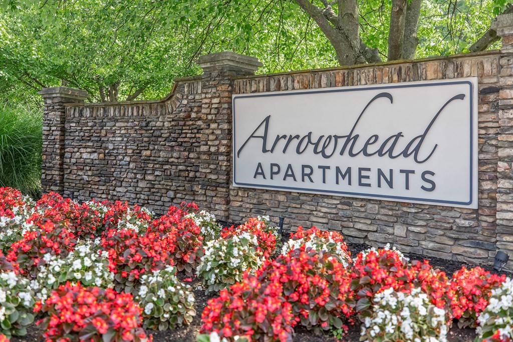 a stone wall with a sign and red and white flowers