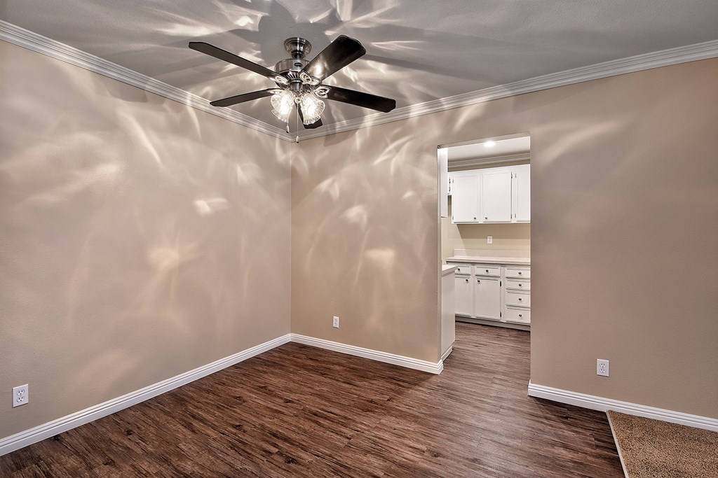 an empty living room with a ceiling fan and a kitchen