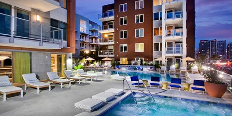 A large outdoor pool with lounge chairs and a hot tub in front of apartment buildings.