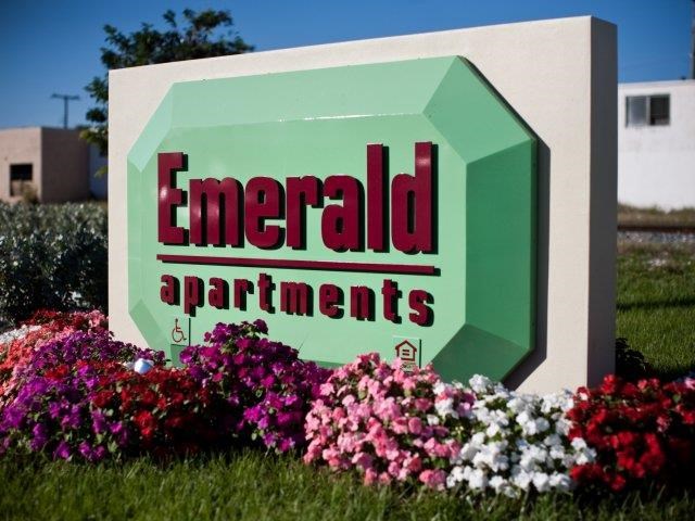 a sign for emerald apartments in a garden of flowers