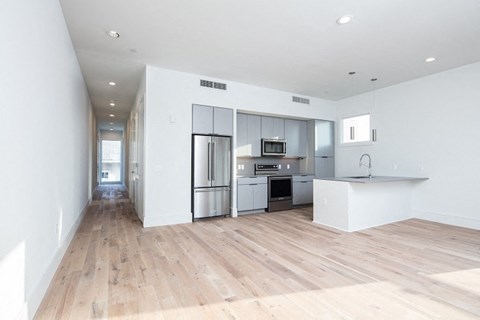 an empty living room with a kitchen with stainless steel appliances