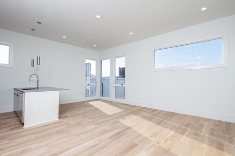 an empty living room with a kitchen and a door to a balcony