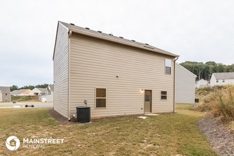 the outside of a small house with a yard and a trash can