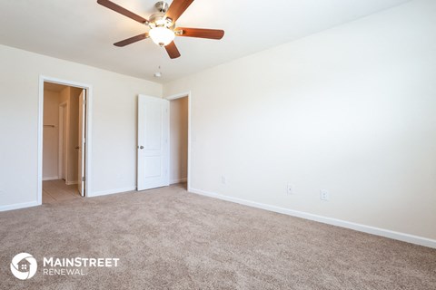 the living room of an apartment with carpet and a ceiling fan