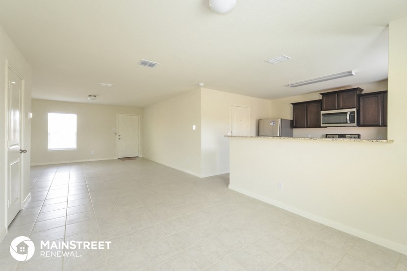 an empty living room and kitchen with white tile flooring and a counter