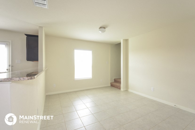an empty living room with tile flooring and a kitchen