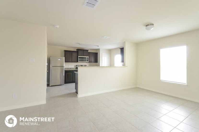 an empty living room with a kitchen in the background