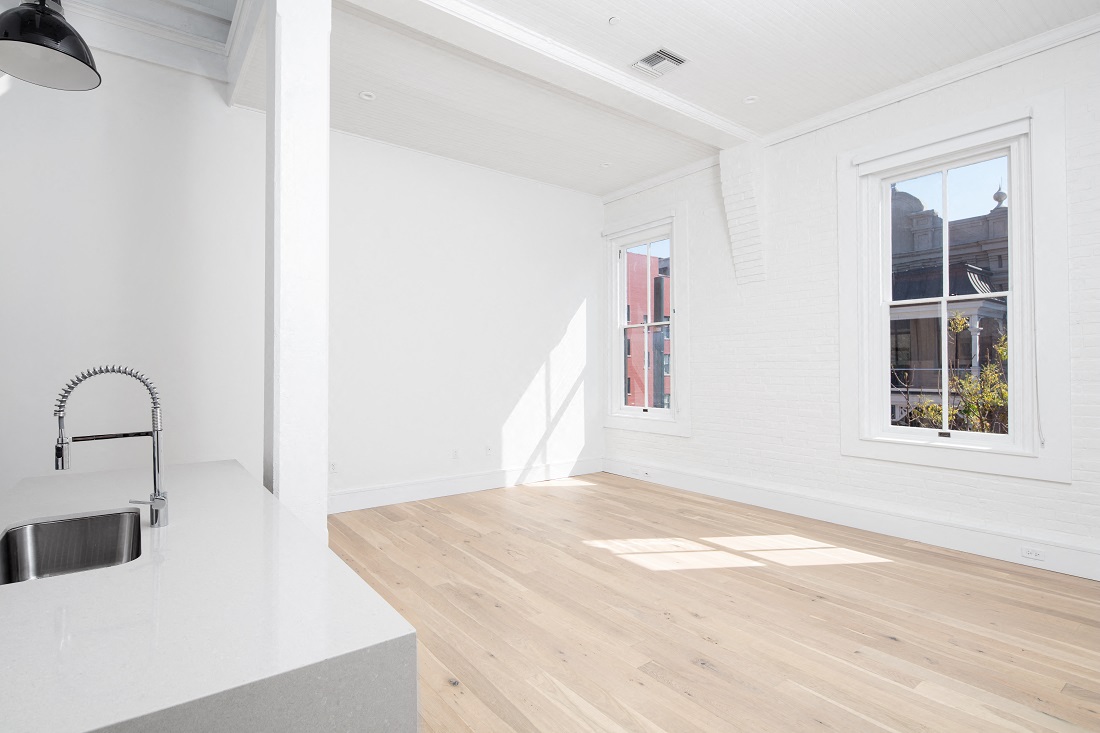 an open kitchen and living room with white walls and wood floors