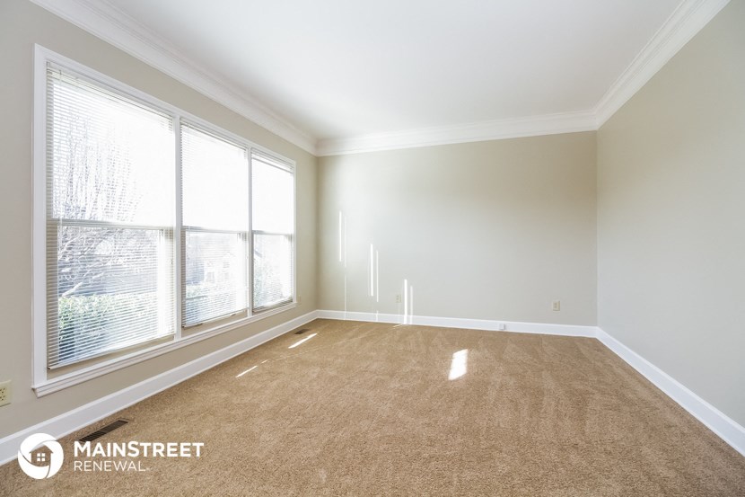an empty living room with three large windows and a carpet
