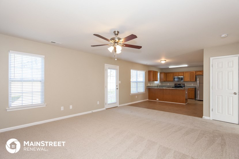 an empty living room with a ceiling fan and a kitchen
