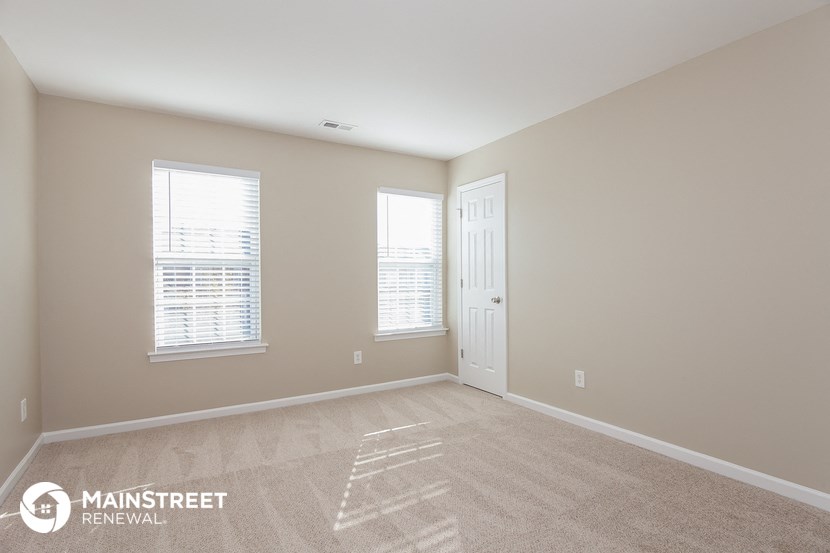 a bedroom with a door and two windows and a carpeted floor