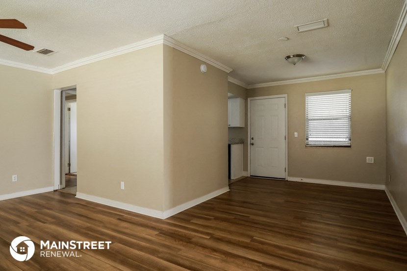 the interior of an empty living room with wooden floors and a door to a kitchen