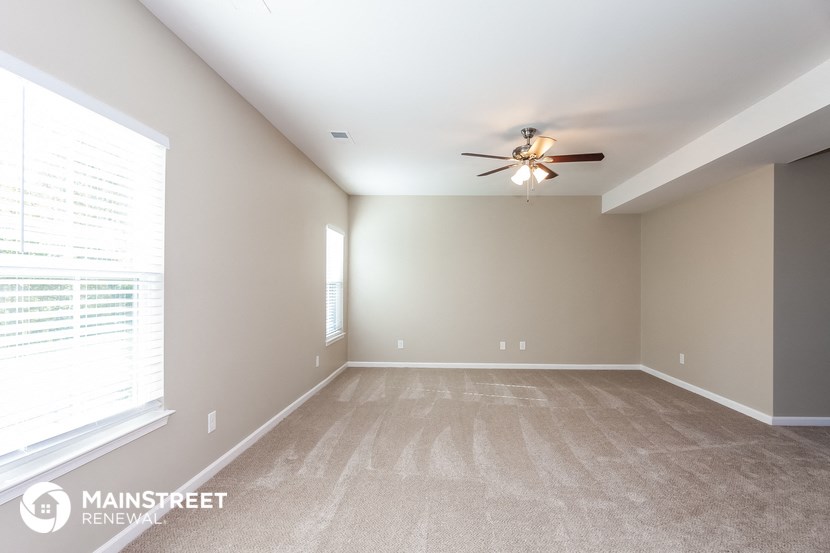 the spacious living room with ceiling fan and large window