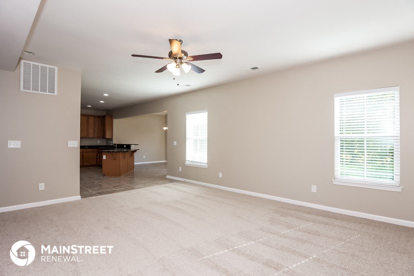 an empty living room with a ceiling fan and a kitchen