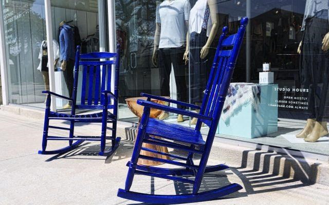two blue rocking chairs on the sidewalk in front of a store