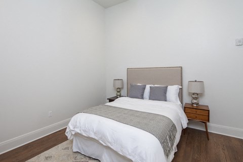 a bedroom with white walls and a bed with a white comforter and gray