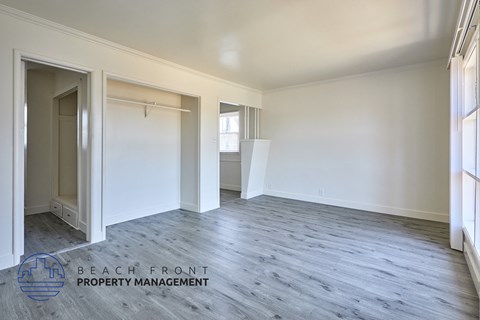 A spacious room with wooden flooring and white walls, with a doorway leading to another room.