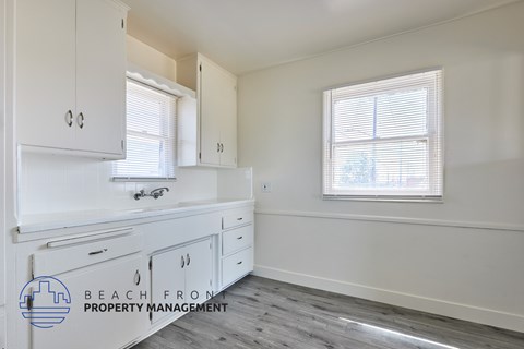 A kitchen with white cabinets and a window with blinds.