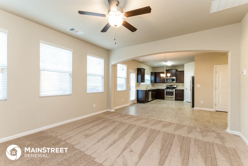 an empty living room with a ceiling fan and a kitchen