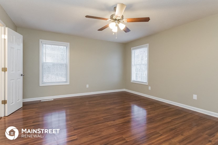 the spacious living room with hardwood flooring and a ceiling fan