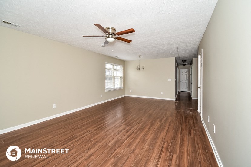 the spacious living room with hardwood flooring and a ceiling fan