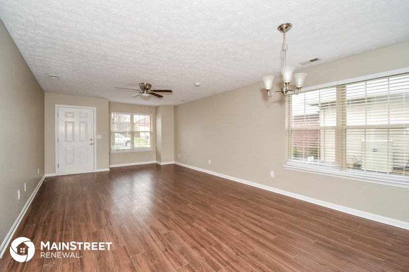 the spacious living room with wood flooring and a ceiling fan