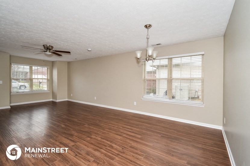 the spacious living room with hardwood flooring and a ceiling fan