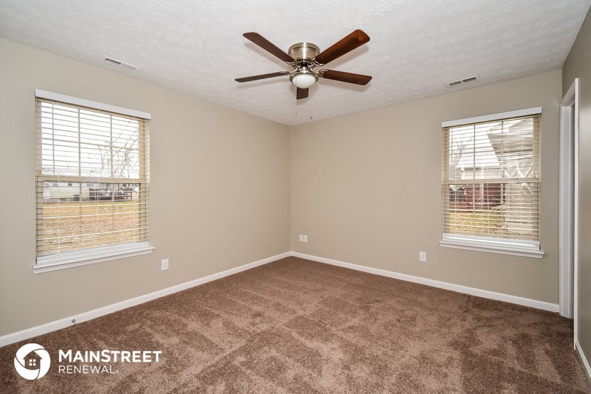 an empty room with a ceiling fan and two windows