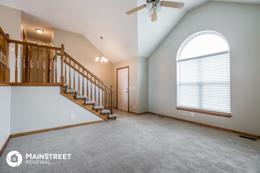 an empty living room with a staircase and a large arched window