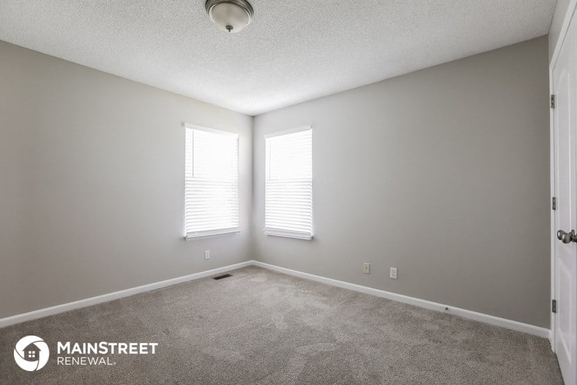 the spacious living room with two windows and carpeting
