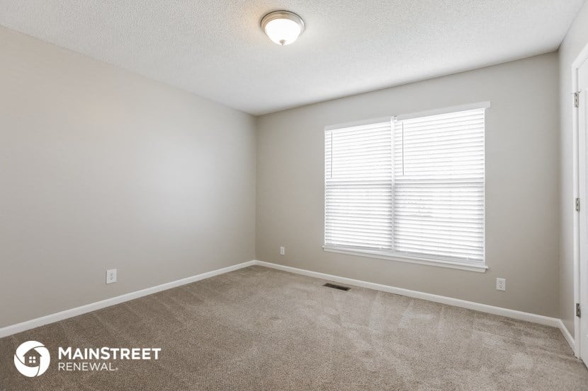 the spacious living room with a large window and carpeted flooring