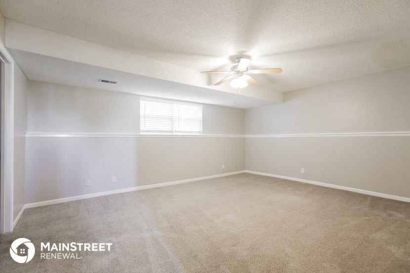 the spacious living room with ceiling fan and carpeting