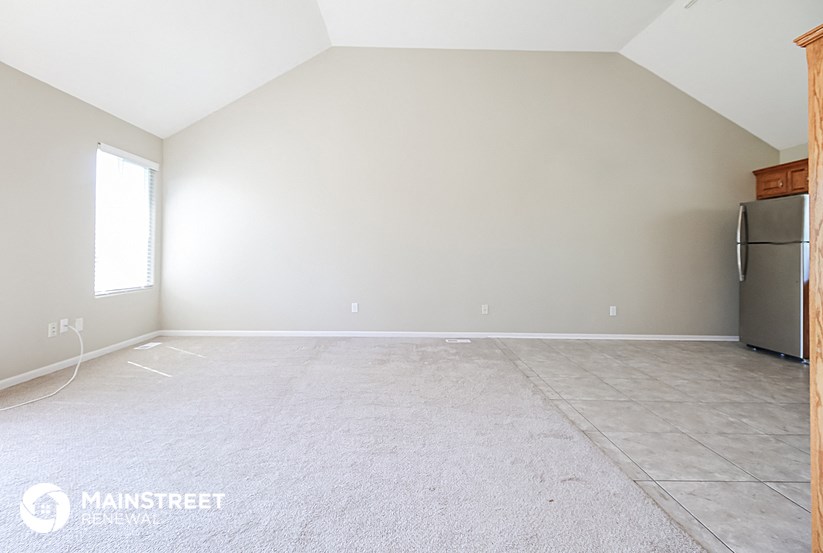 an empty living room with a refrigerator and tile floor