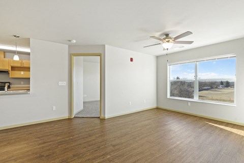 an empty living room with a large window and a ceiling fan