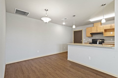 the living room and kitchen of an empty apartment with wood flooring and white walls