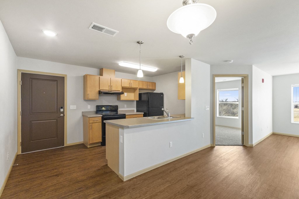 an empty living room with a kitchen and a door to a hallway