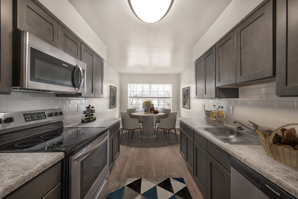 a kitchen with stainless steel appliances and gray cabinets and a dining room with a window